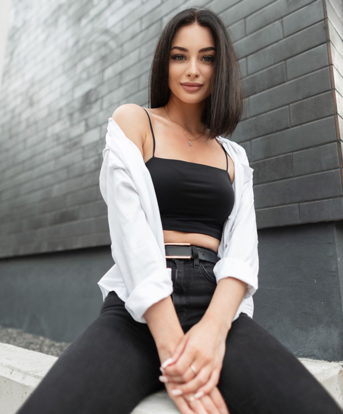 Woman sitting against gray wall, casual fashion.