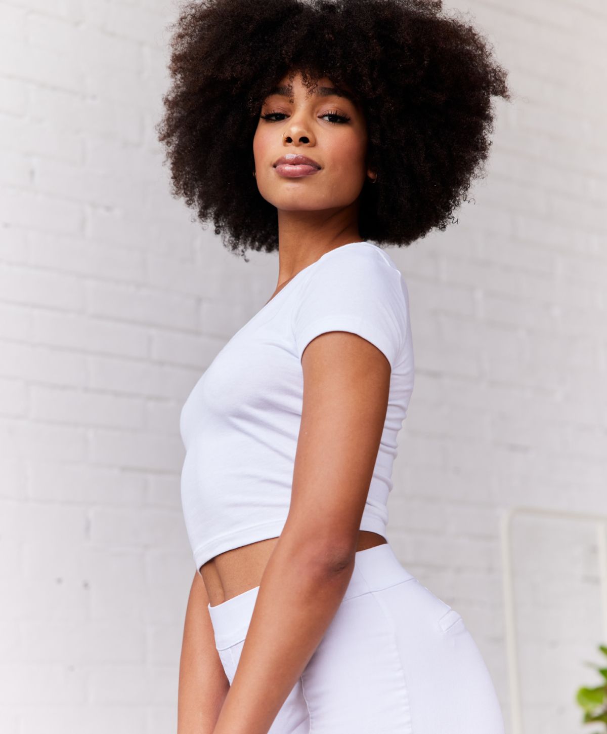Woman with curly hair posing in a white outfit.