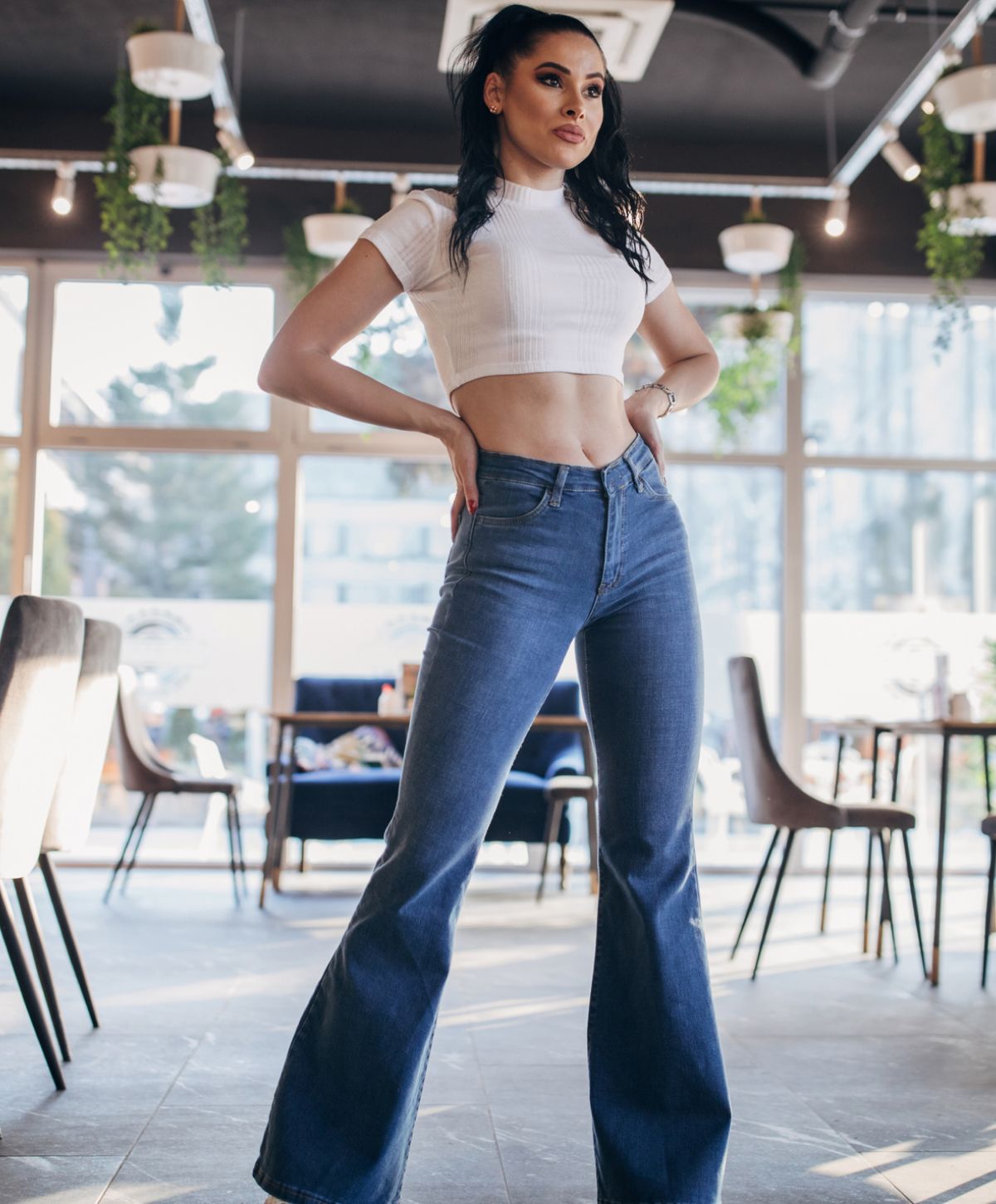 Woman in crop top and flared jeans posing indoors.