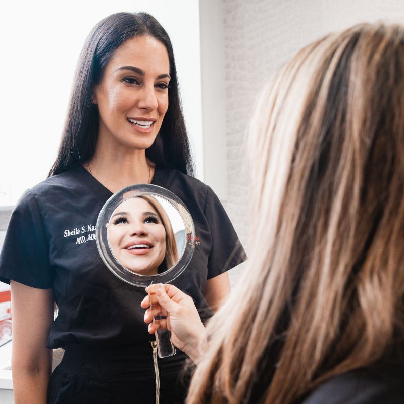Woman examines her reflection in a handheld mirror.