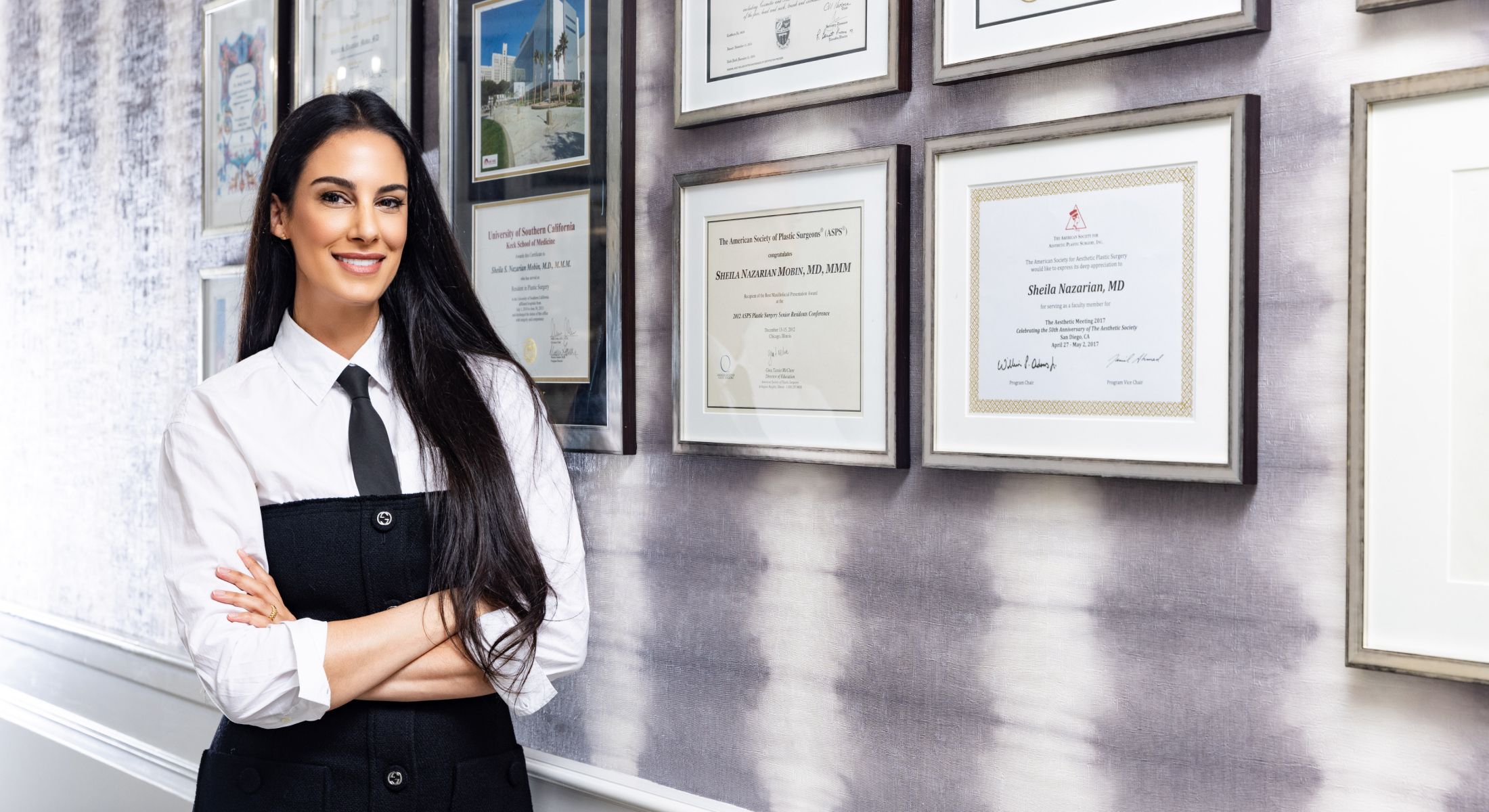 Professional woman posing by framed certificates.