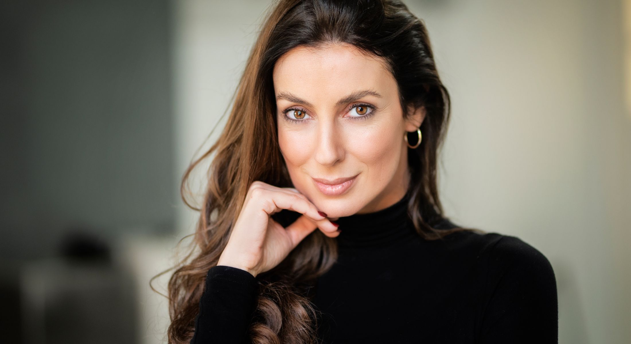 Woman smiling, hand on chin, black turtleneck.