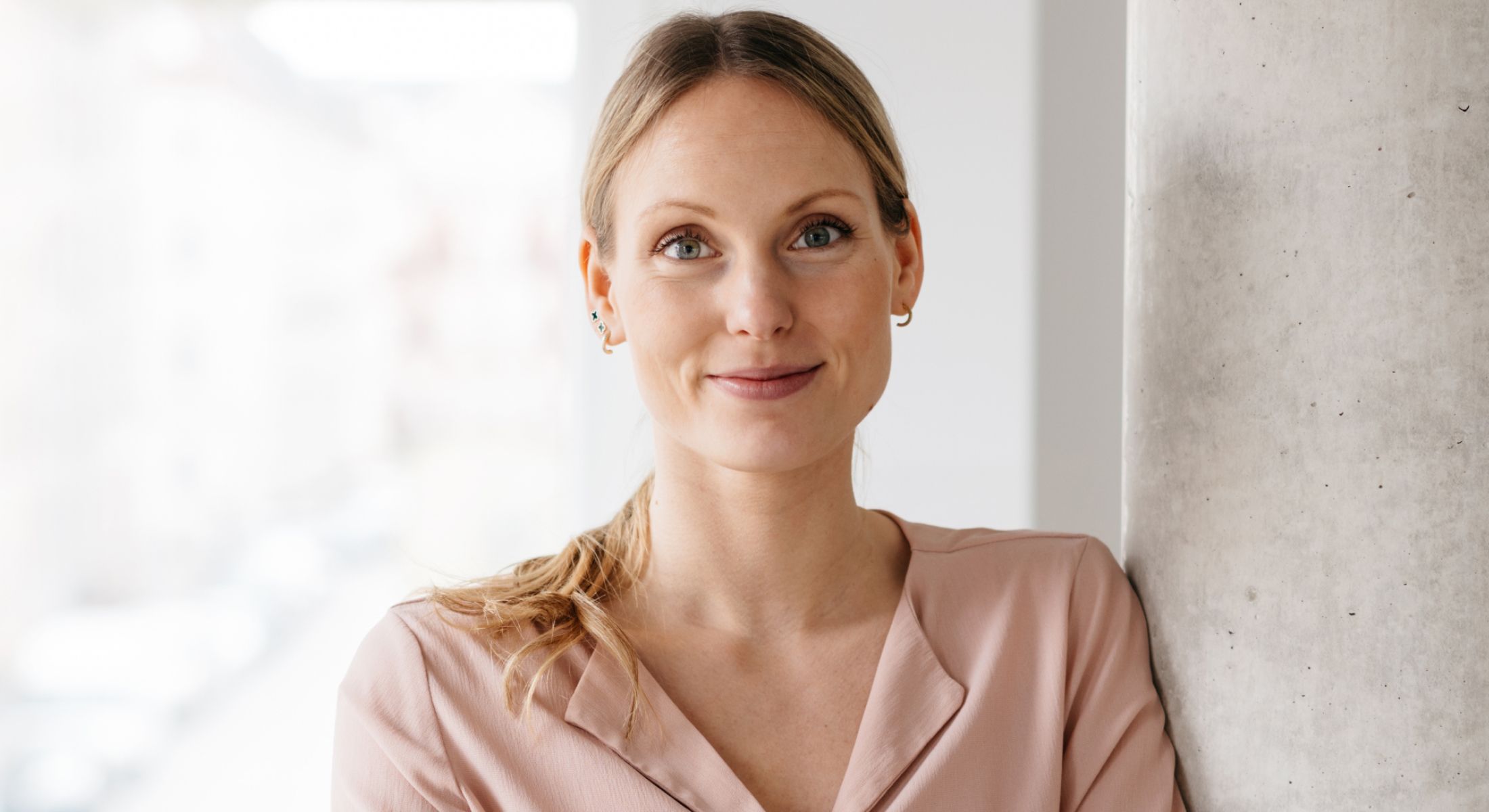 Smiling woman leaning against concrete pillar.