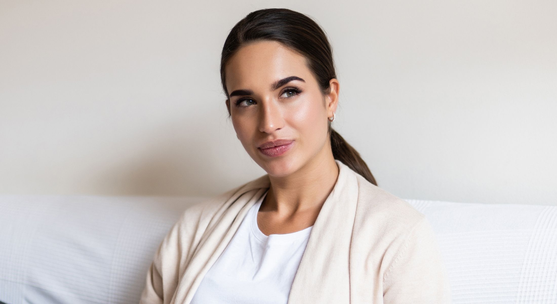 Woman thoughtfully gazing while seated on couch.