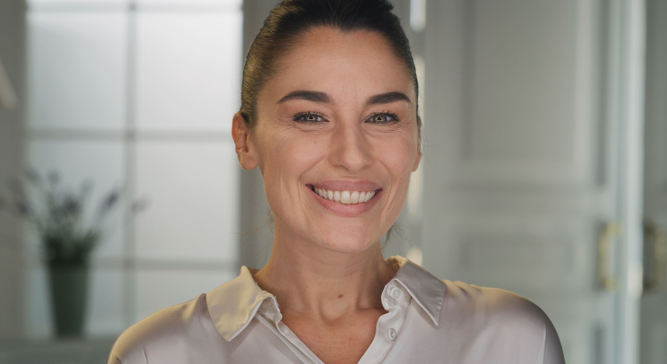 Smiling woman in a light blouse, soft background.