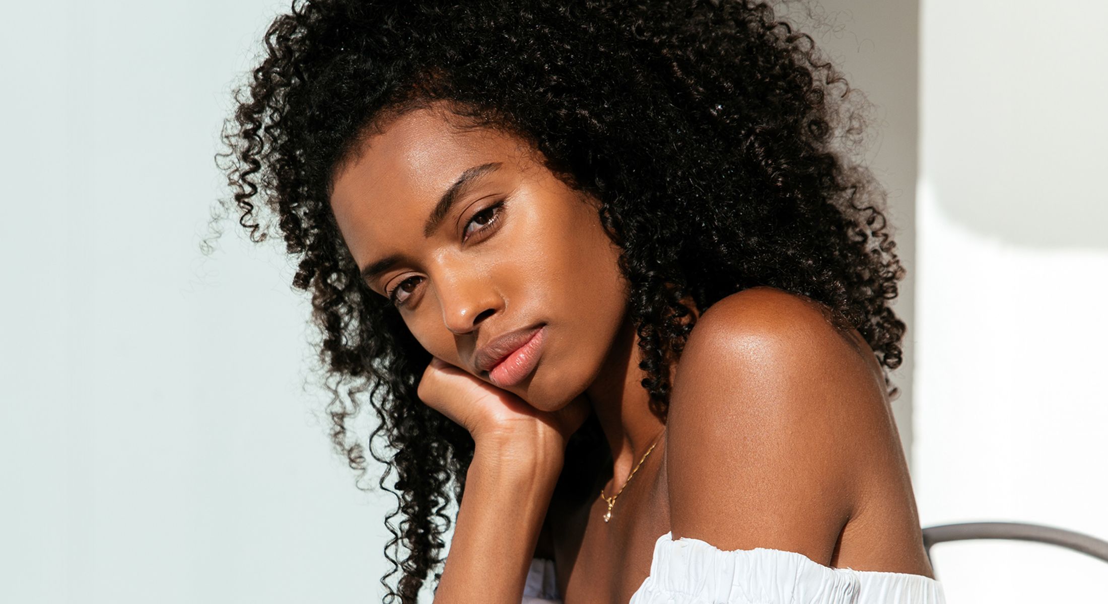 Woman with curly hair resting her chin on hand.